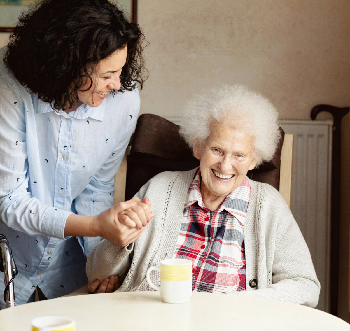 Hispanic caregiver smiling and helping an elderly lady drinking tea